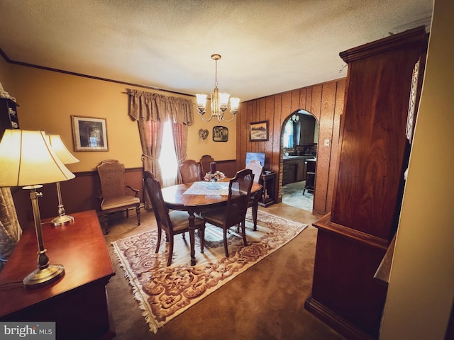 dining room featuring wooden walls, carpet floors, a textured ceiling, and an inviting chandelier