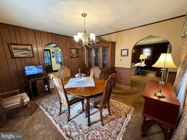 carpeted dining room with a notable chandelier, wood walls, and a textured ceiling