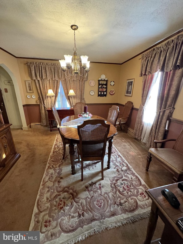 carpeted dining room with a textured ceiling, an inviting chandelier, and ornamental molding