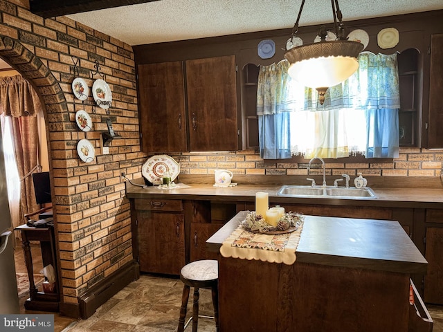 kitchen with dark brown cabinetry, sink, pendant lighting, and a textured ceiling