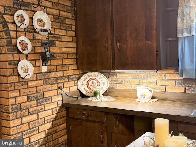 interior space with butcher block countertops, dark brown cabinets, and brick wall