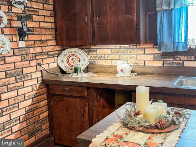 kitchen with dark brown cabinetry, wooden counters, and brick wall