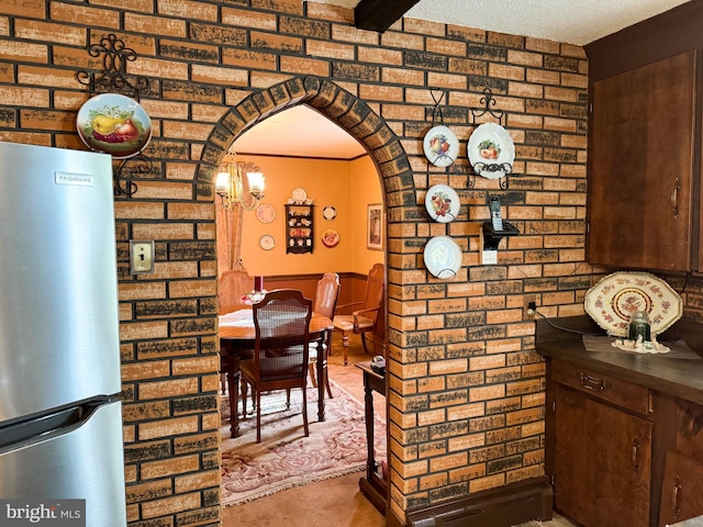 unfurnished dining area with light carpet, a textured ceiling, brick wall, and a chandelier