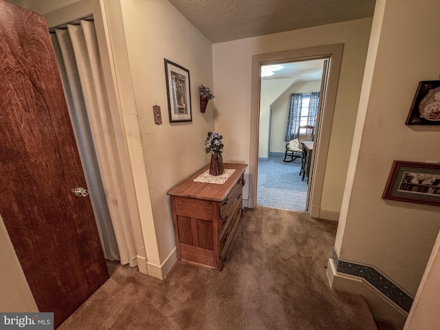 hallway featuring dark carpet and a textured ceiling