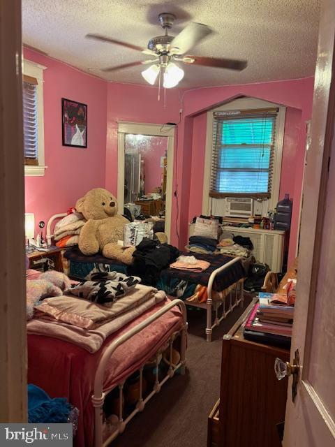 bedroom featuring dark colored carpet, ceiling fan, cooling unit, and a textured ceiling