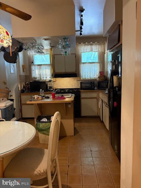 kitchen featuring black refrigerator, decorative backsplash, white cabinetry, and light tile patterned floors