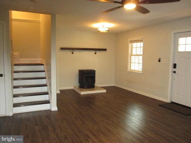 unfurnished living room with a healthy amount of sunlight, a wood stove, ceiling fan, and dark wood-type flooring