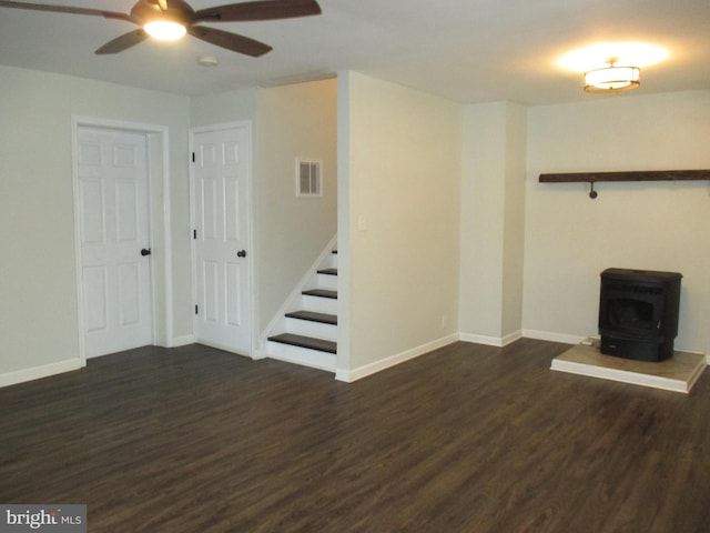 unfurnished living room with dark hardwood / wood-style flooring, a wood stove, and ceiling fan