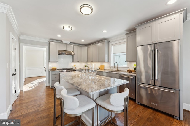 kitchen with a kitchen bar, sink, a kitchen island, light stone counters, and stainless steel appliances