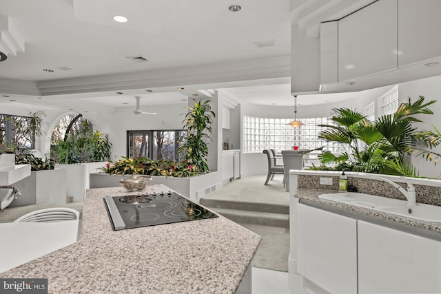 kitchen featuring white cabinets, sink, ceiling fan, black electric cooktop, and light stone counters