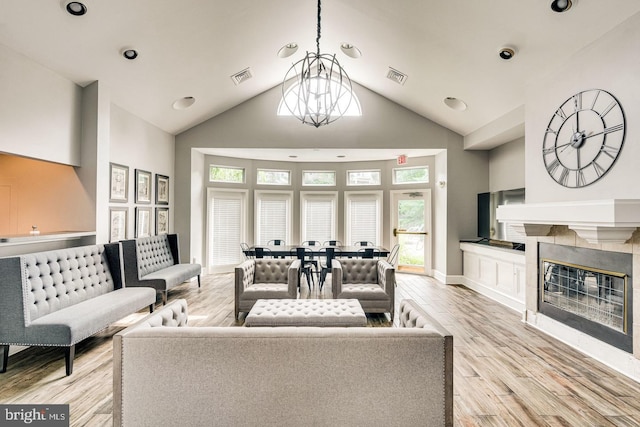 living room featuring a fireplace, high vaulted ceiling, a chandelier, and light wood-type flooring