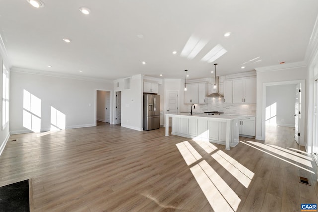 kitchen featuring stainless steel refrigerator with ice dispenser, a kitchen island with sink, wall chimney range hood, light hardwood / wood-style floors, and white cabinetry