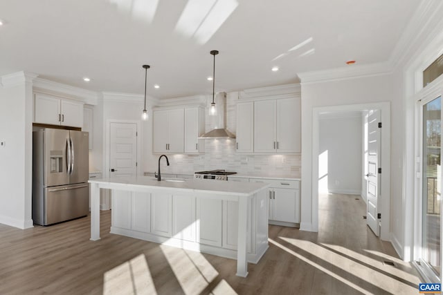 kitchen featuring appliances with stainless steel finishes, a kitchen island with sink, sink, wall chimney range hood, and light hardwood / wood-style flooring