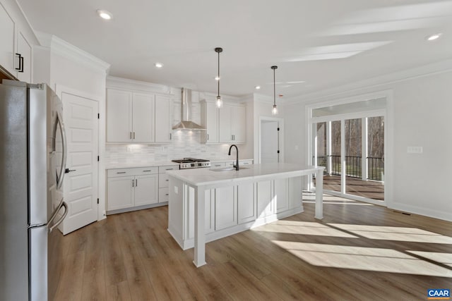 kitchen featuring wall chimney exhaust hood, white cabinetry, a kitchen island with sink, and appliances with stainless steel finishes