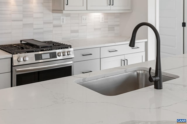 kitchen with backsplash, light stone countertops, sink, and stainless steel range