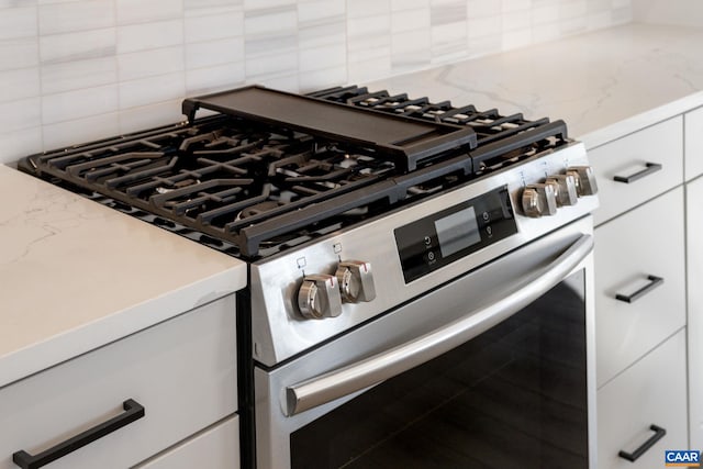 room details featuring white cabinets, decorative backsplash, light stone counters, and stainless steel stove