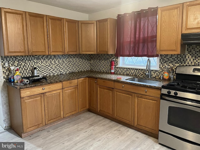 kitchen with gas range, sink, light hardwood / wood-style flooring, extractor fan, and decorative backsplash