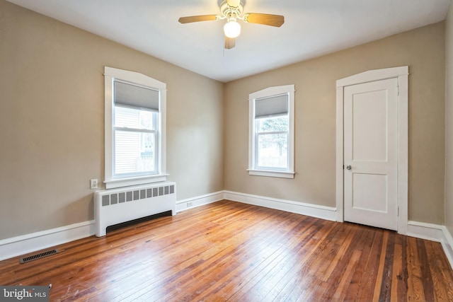 empty room with radiator heating unit, hardwood / wood-style flooring, and ceiling fan