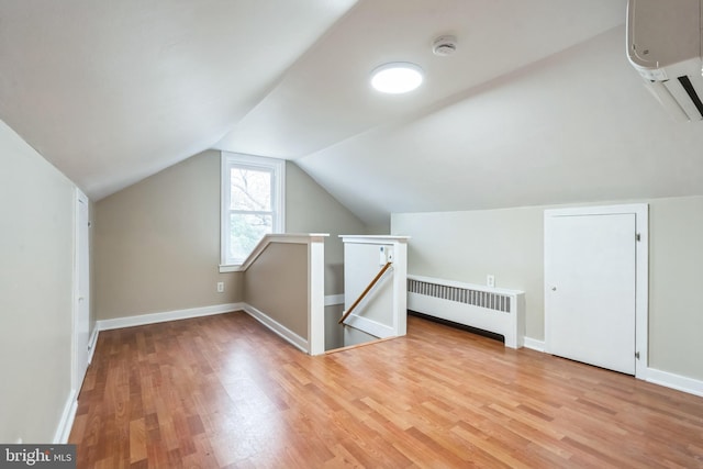 bonus room with radiator heating unit, light hardwood / wood-style floors, vaulted ceiling, and an AC wall unit