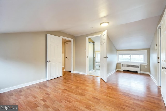 additional living space with radiator heating unit, light hardwood / wood-style flooring, and vaulted ceiling