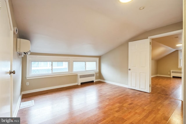 additional living space featuring radiator heating unit, vaulted ceiling, light hardwood / wood-style floors, and an AC wall unit