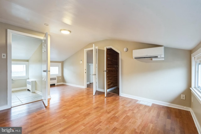 additional living space featuring a wall mounted air conditioner, light wood-type flooring, radiator, and vaulted ceiling