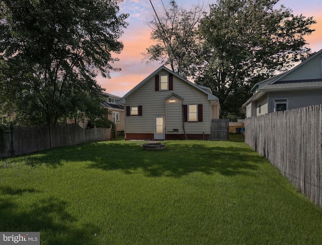 back house at dusk featuring a fire pit and a lawn