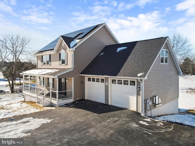 view of snowy exterior with covered porch, solar panels, and a garage