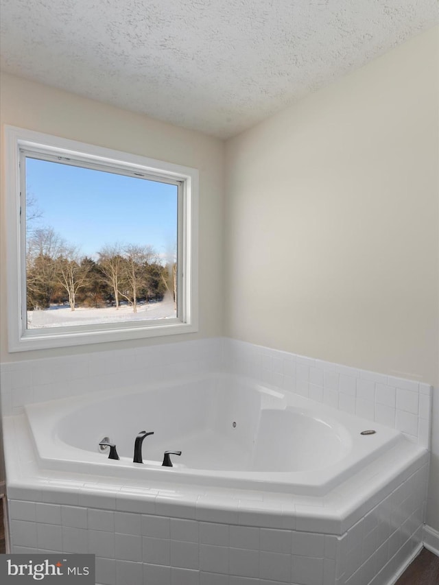 bathroom with tiled tub and a textured ceiling