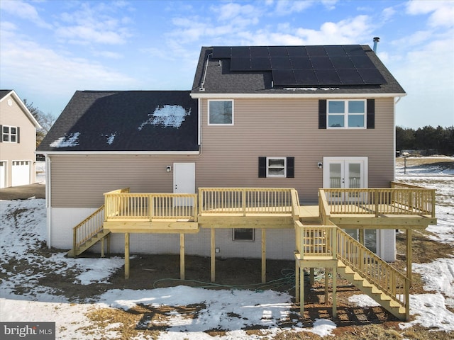 snow covered property with french doors, a wooden deck, and solar panels