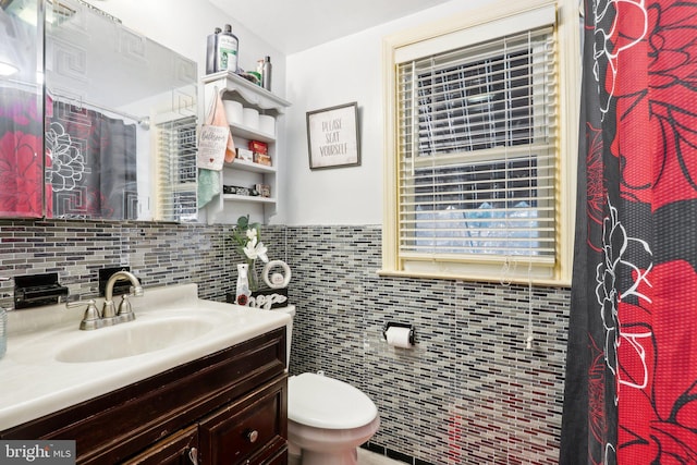 bathroom with walk in shower, vanity, tile walls, and toilet