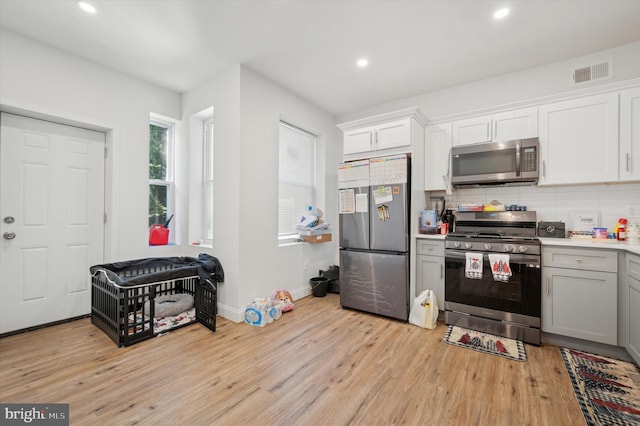 kitchen with white cabinets, light hardwood / wood-style flooring, stainless steel appliances, and tasteful backsplash