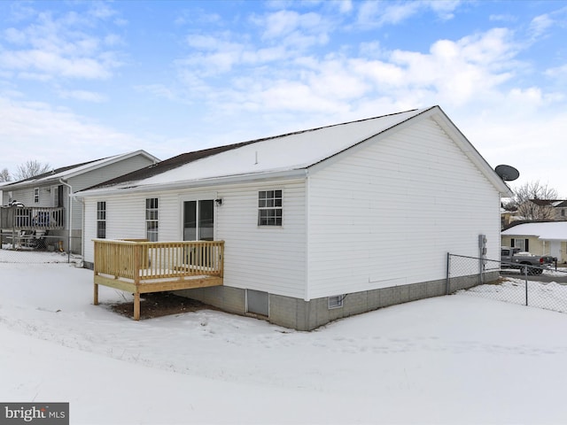 snow covered back of property with a wooden deck