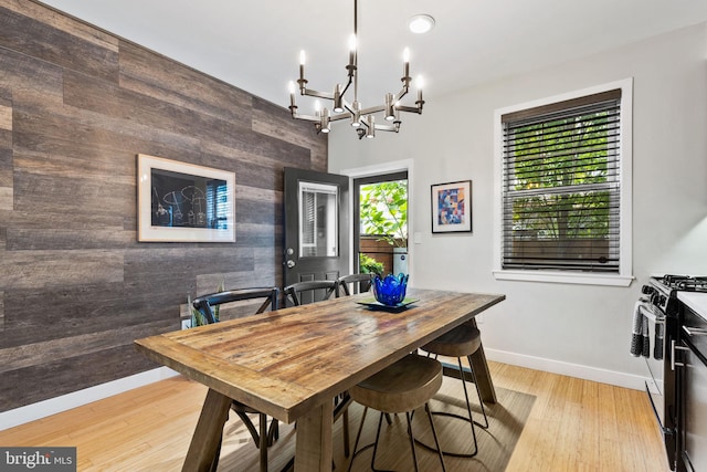 dining room with wood walls, an inviting chandelier, and light hardwood / wood-style flooring