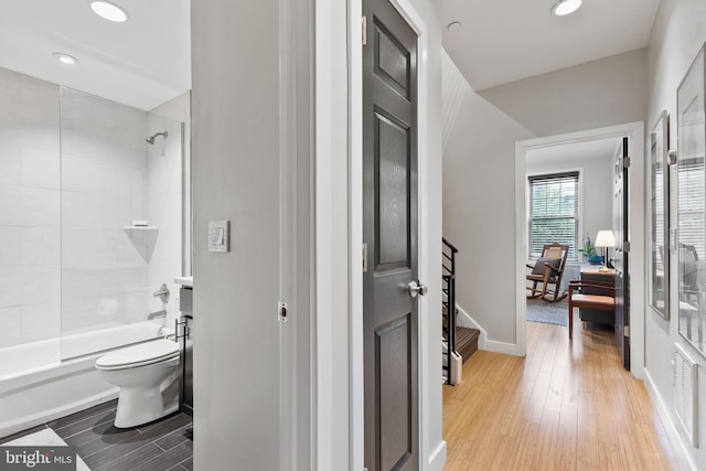 bathroom with wood-type flooring, toilet, and tiled shower / bath