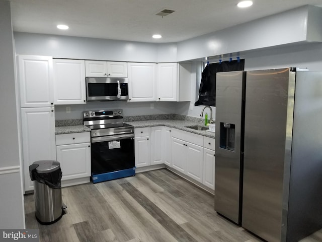 kitchen with white cabinets, sink, light hardwood / wood-style flooring, light stone counters, and stainless steel appliances