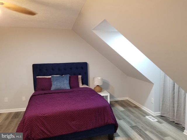 bedroom featuring ceiling fan, wood-type flooring, and lofted ceiling with skylight