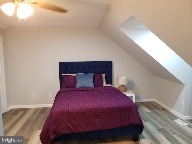 bedroom featuring hardwood / wood-style floors, lofted ceiling with skylight, and ceiling fan