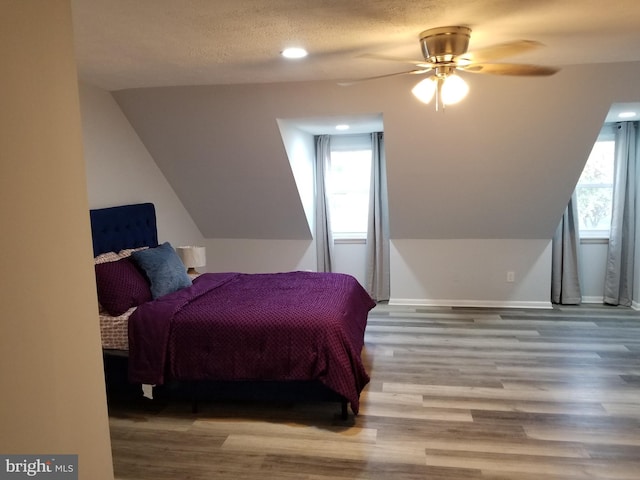 bedroom featuring multiple windows, light hardwood / wood-style flooring, ceiling fan, and lofted ceiling