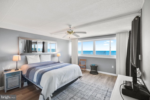 bedroom with hardwood / wood-style floors, a textured ceiling, a water view, and ceiling fan