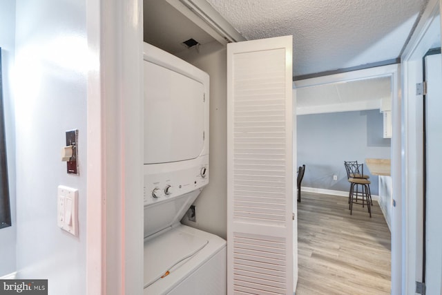 laundry area featuring a textured ceiling, light hardwood / wood-style flooring, and stacked washer / dryer