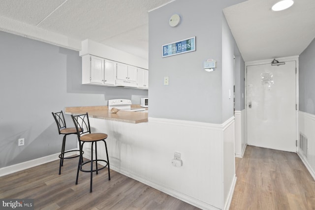 kitchen with stove, white cabinets, a kitchen breakfast bar, light wood-type flooring, and kitchen peninsula