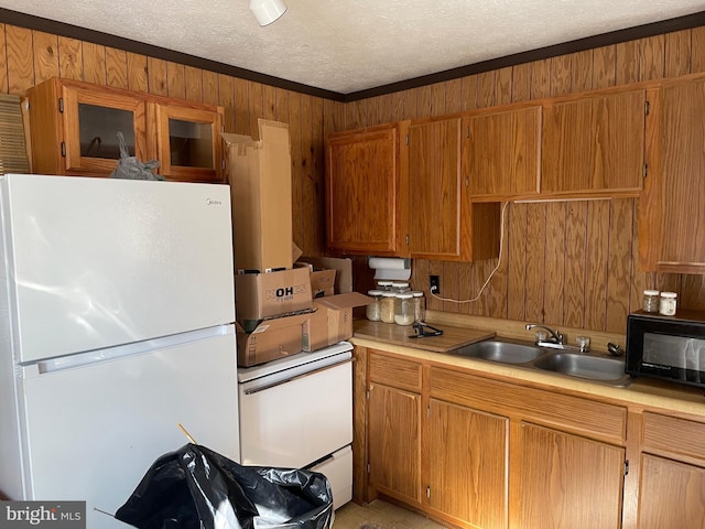 kitchen with a textured ceiling, white refrigerator, wooden walls, sink, and crown molding