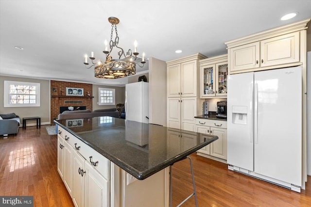 kitchen featuring a brick fireplace, white fridge with ice dispenser, cream cabinetry, and hanging light fixtures