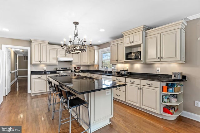 kitchen with stainless steel range with electric cooktop, hanging light fixtures, a kitchen island, cream cabinets, and sink