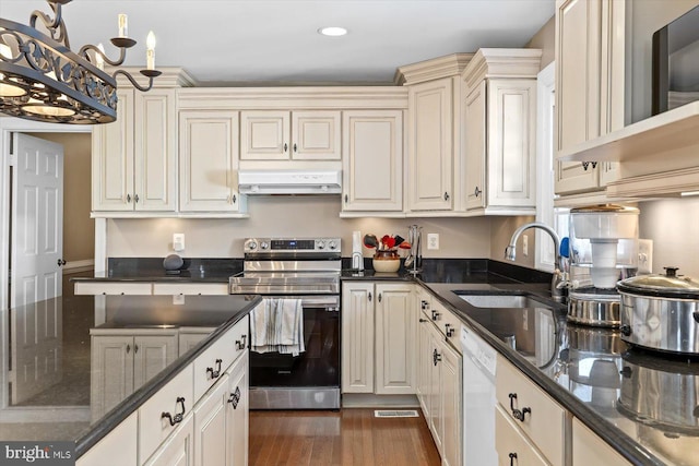 kitchen with dark stone countertops, pendant lighting, electric range, sink, and cream cabinetry