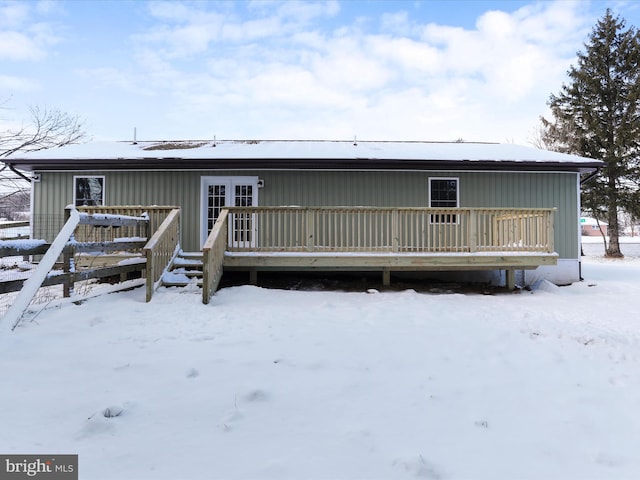 snow covered property with a wooden deck and french doors