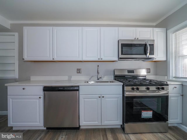 kitchen with white cabinets, sink, ornamental molding, appliances with stainless steel finishes, and dark hardwood / wood-style flooring