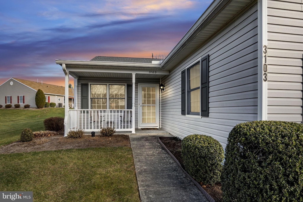 exterior entry at dusk with a porch and a lawn