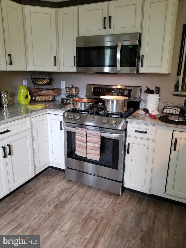 kitchen with light stone counters, white cabinets, stainless steel appliances, and wood-type flooring